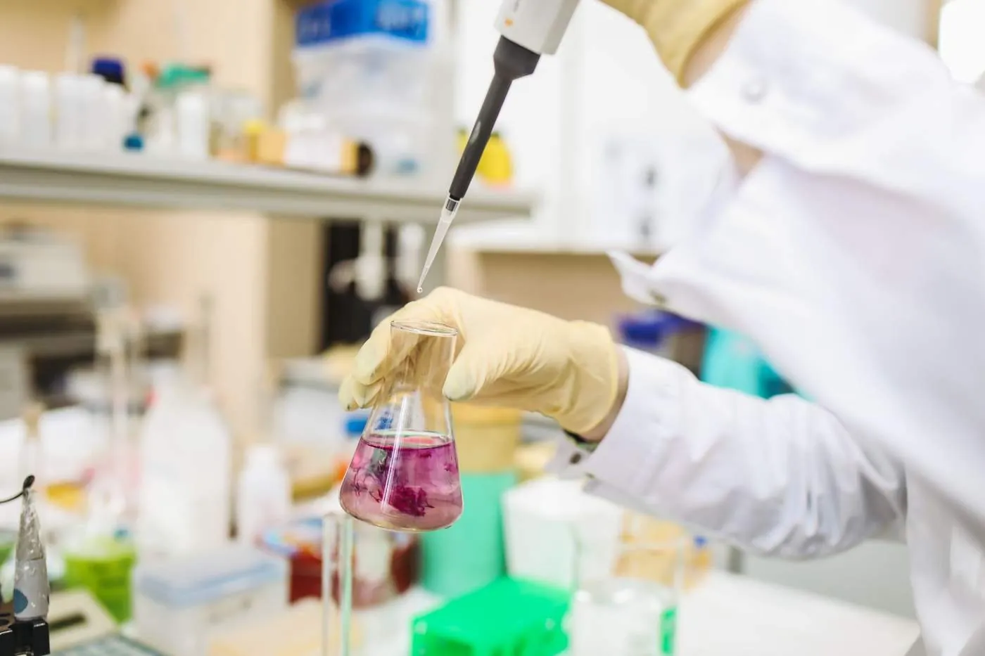 A scientist in gloves using a pipette over a flask in a laboratory