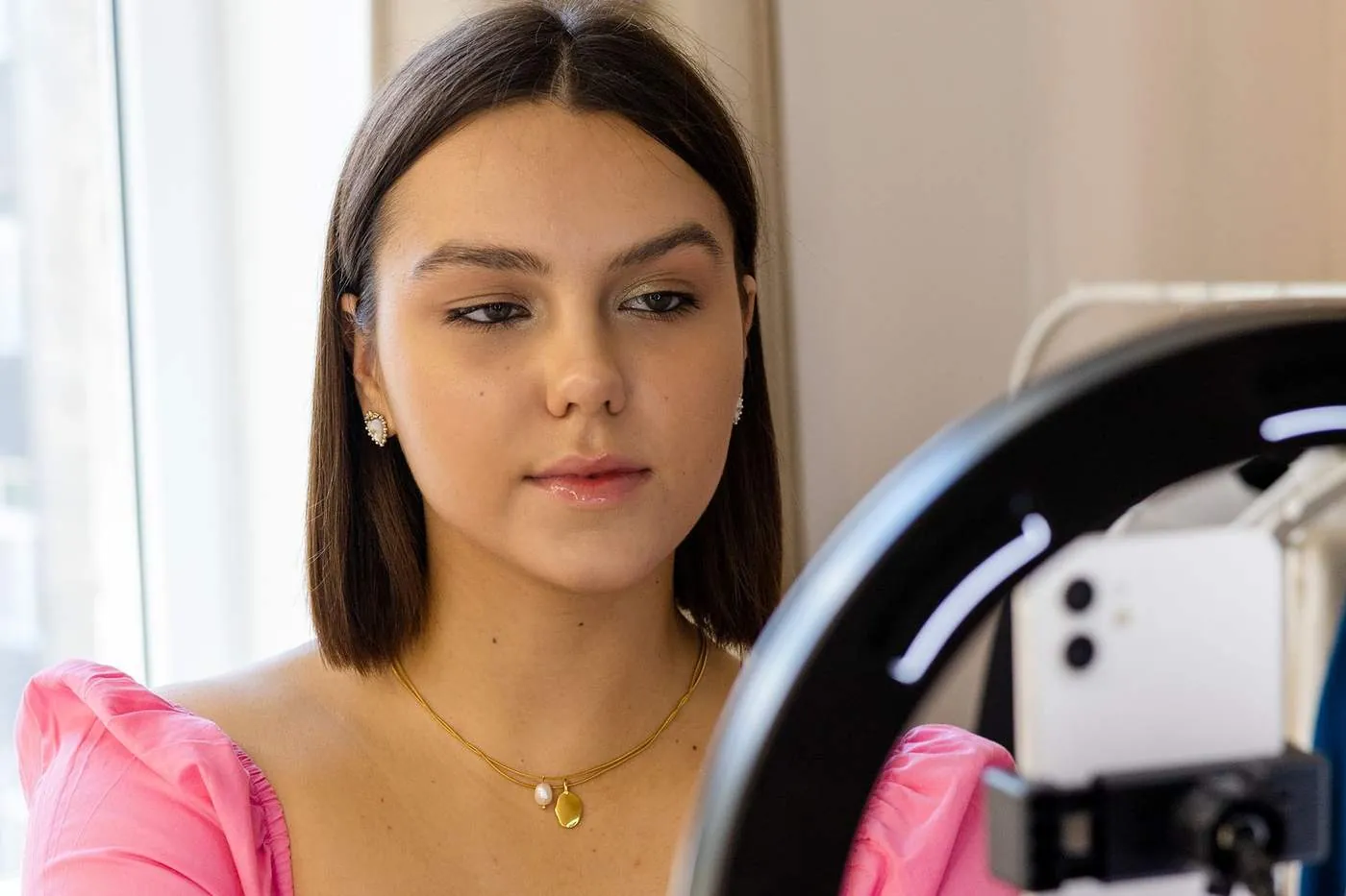 A woman setting up a smartphone in a ring light to film a video