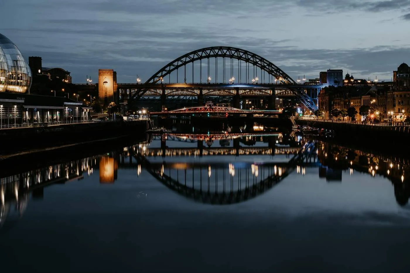 The Tyne Bridge lit up at night, reflected in the River Tyne